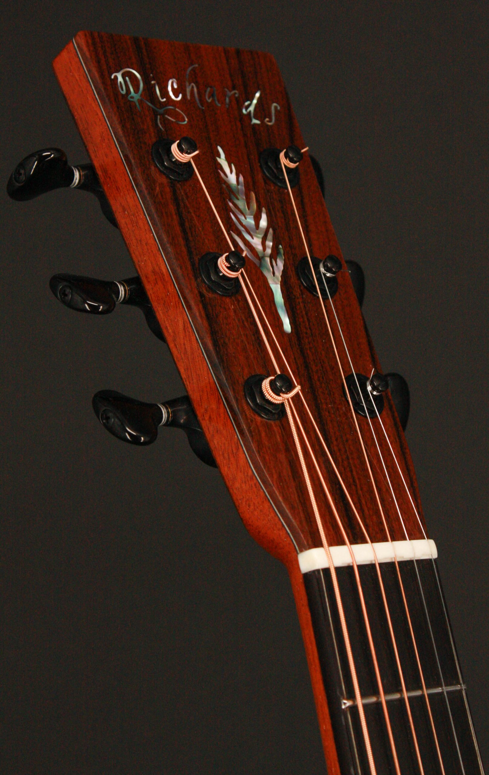 Close-up of a wooden guitar headstock with tuning pegs, featuring the name "Richards" and a decorative inlay design.