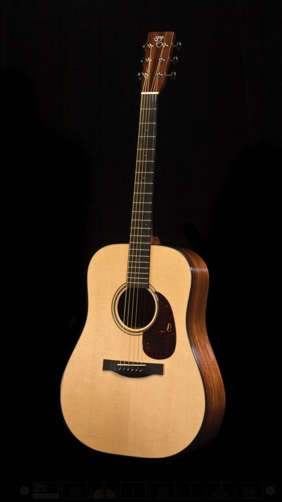 Acoustic guitar with a natural wood finish, dark wooden sides, six strings, and a tortoiseshell pickguard, photographed against a black background.