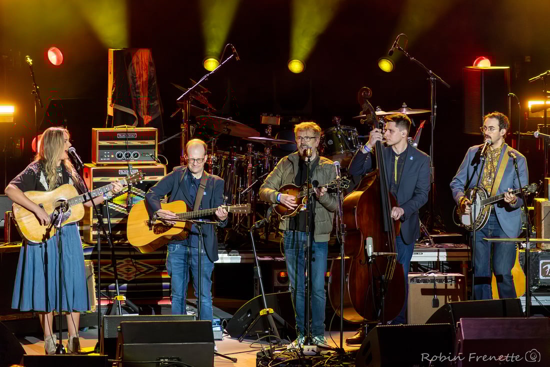 Spectrum Bluegrass Band at Greek Theater - Robin Frenette Five musicians perform on stage with guitars, a mandolin, and a double bass, surrounded by musical equipment and illuminated by stage lights.