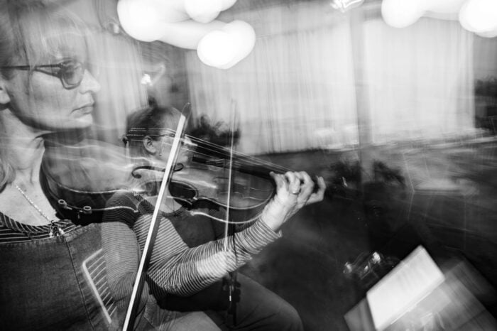 A black and white photo shows a woman playing a violin, with motion blur creating a sense of movement and overlapping images.
