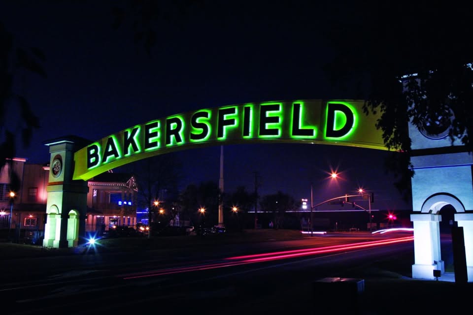 A large illuminated archway sign with the word "Bakersfield" in green letters spanning a street at night.