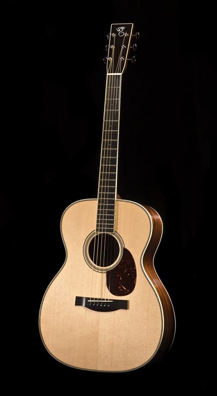 An acoustic guitar with a natural wood finish, dark sides, and a pickguard, set against a black background.
