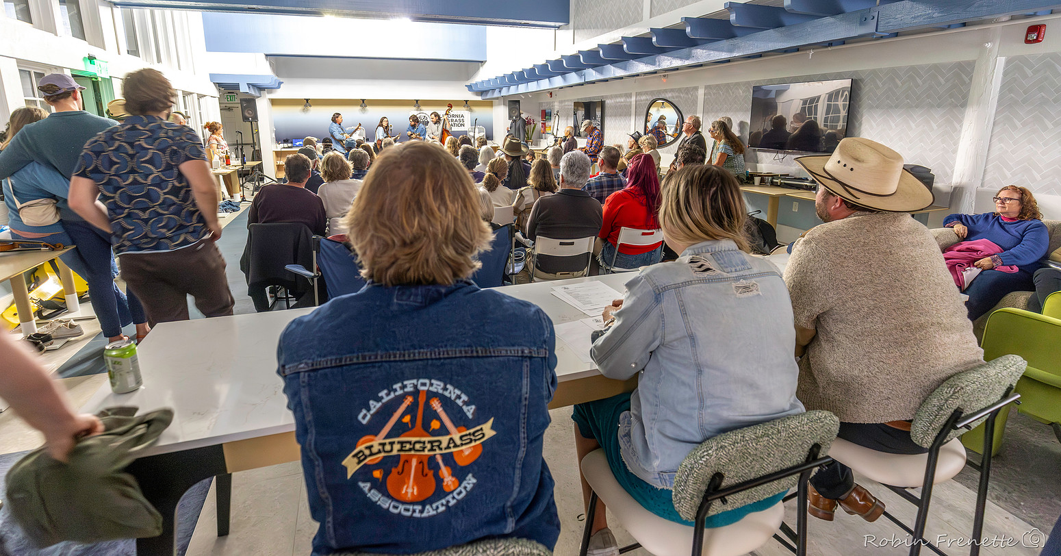 2025 South State 48 A group of people sit and watch a live musical performance in a bright indoor space; some audience members are seated at tables.