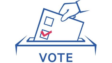 A hand places a ballot with a checked box into a ballot box. The word “VOTE” appears below the box.